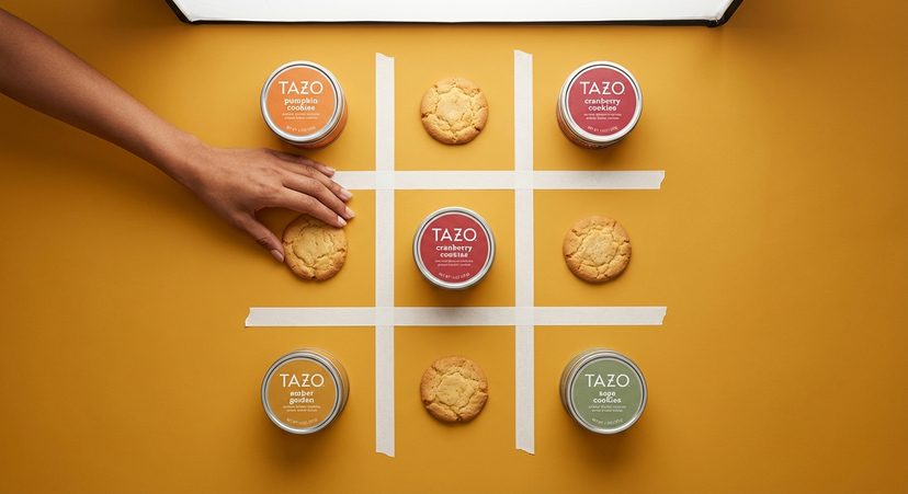 Tazo Tea Biscuit Ad Creative — {'subject': {'description': 'Top-down flat-lay product photography featuring Tazo Tea metal tins and golden round biscuits arrang